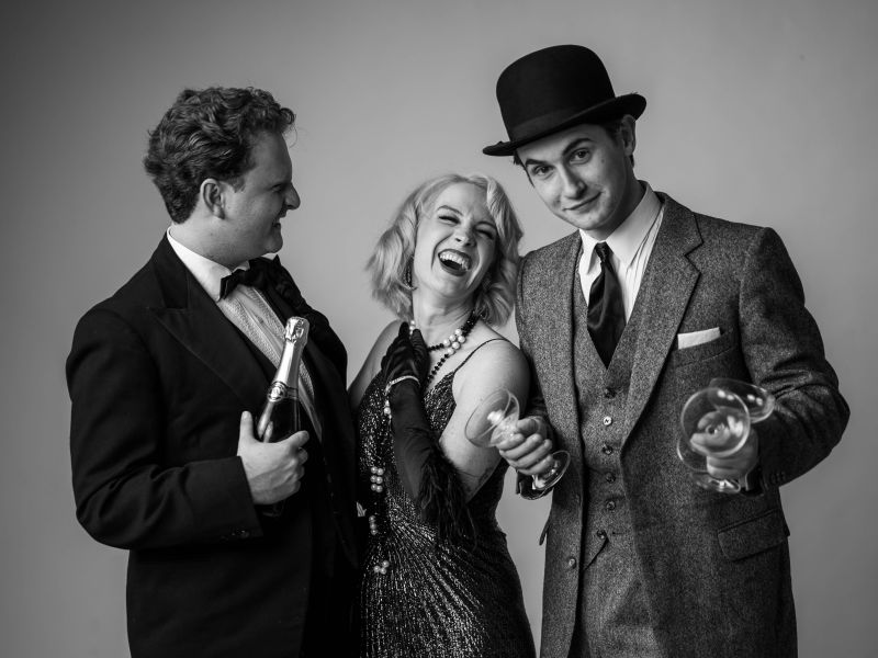 A black and white photo of three people in 1920s clothing, drinking champagne