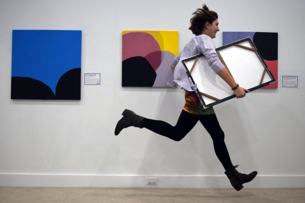 A photo of a woman running through a gallery, clutching a canvas.